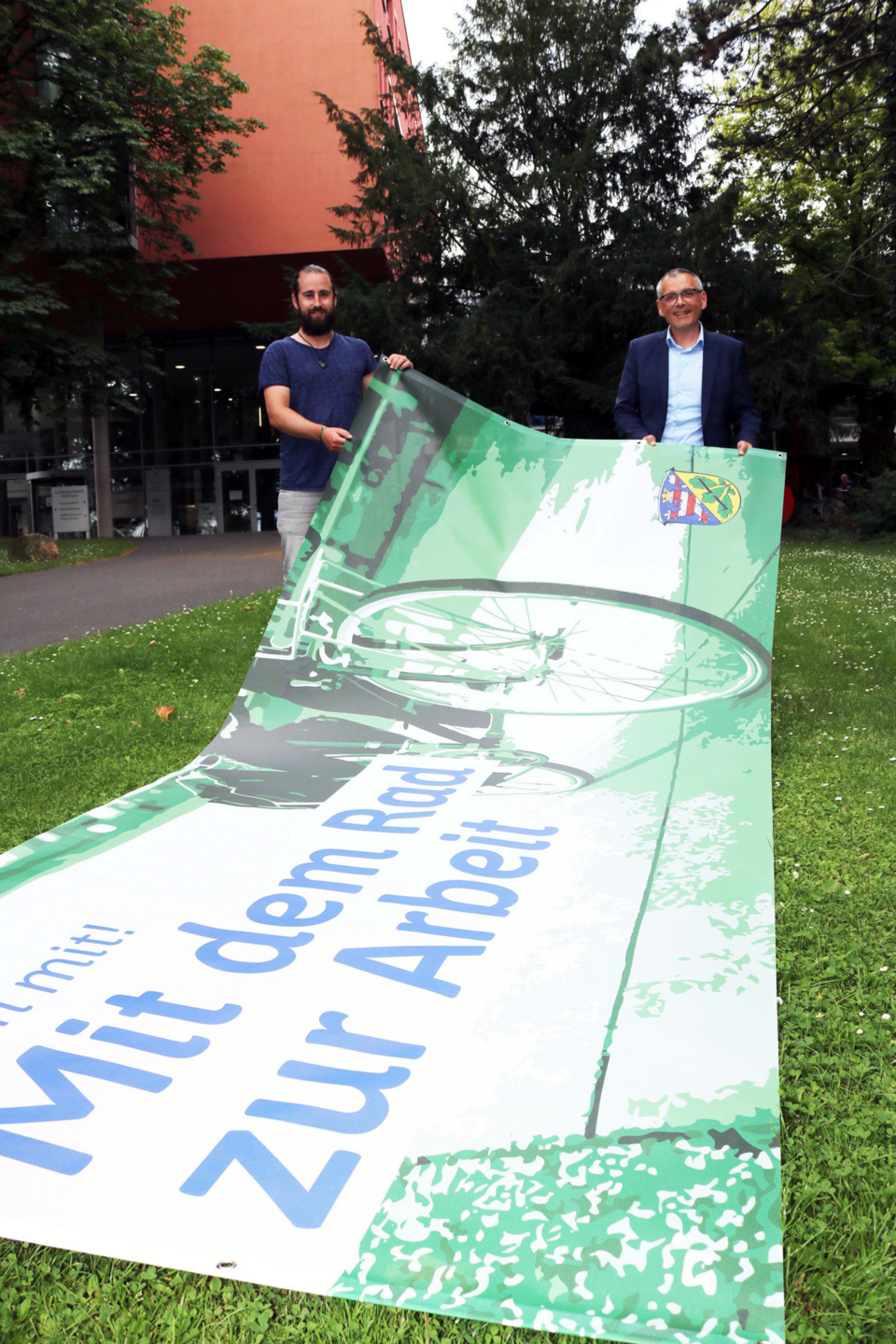 Ein neues Banner zur Aktion „Mit dem Rad zur Arbeit“ schmückt das Kreishaus. Im Bild: Der Radverkehrsbeauftragte Stefan Arend (links) und Vizelandrat Andreas Siebert.