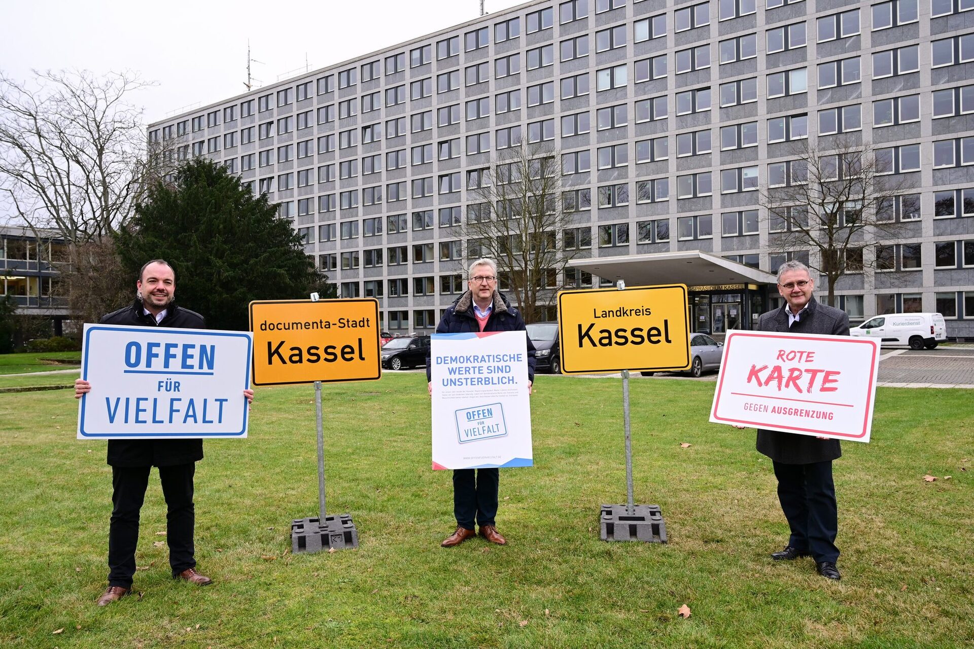 von links nach rechts: Kassels Oberbürgermeister Christian Geselle, Regierungspräsident Hermann-Josef Klüber und Uwe Schmidt, Landrat des Landkreises Kassel, stehen mit Plakaten der Initiative "Offen für Vielfalt" auf der Wiese vor dem Regierungspräsidium.