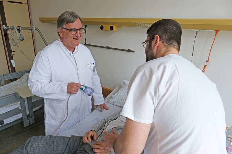 Prof. Dr. Jürgen Fass gemeinsam mit Pfleger Abdo am Patientenbett des Bauchspeicheldrüsenpatienten.